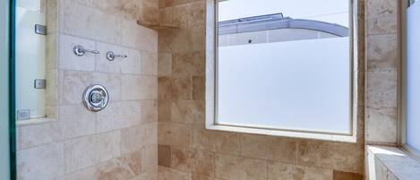 Ducha con puerta de vidrio, ventana y pared con azulejos.