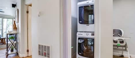 A laundry room with stacked washers and dryers, a vent on the wall, and a chair.
