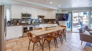 A modern kitchen with white cabinets, a wooden dining table, and a TV mounted on the wall. - Ocean Breeze 1 (San Diego)