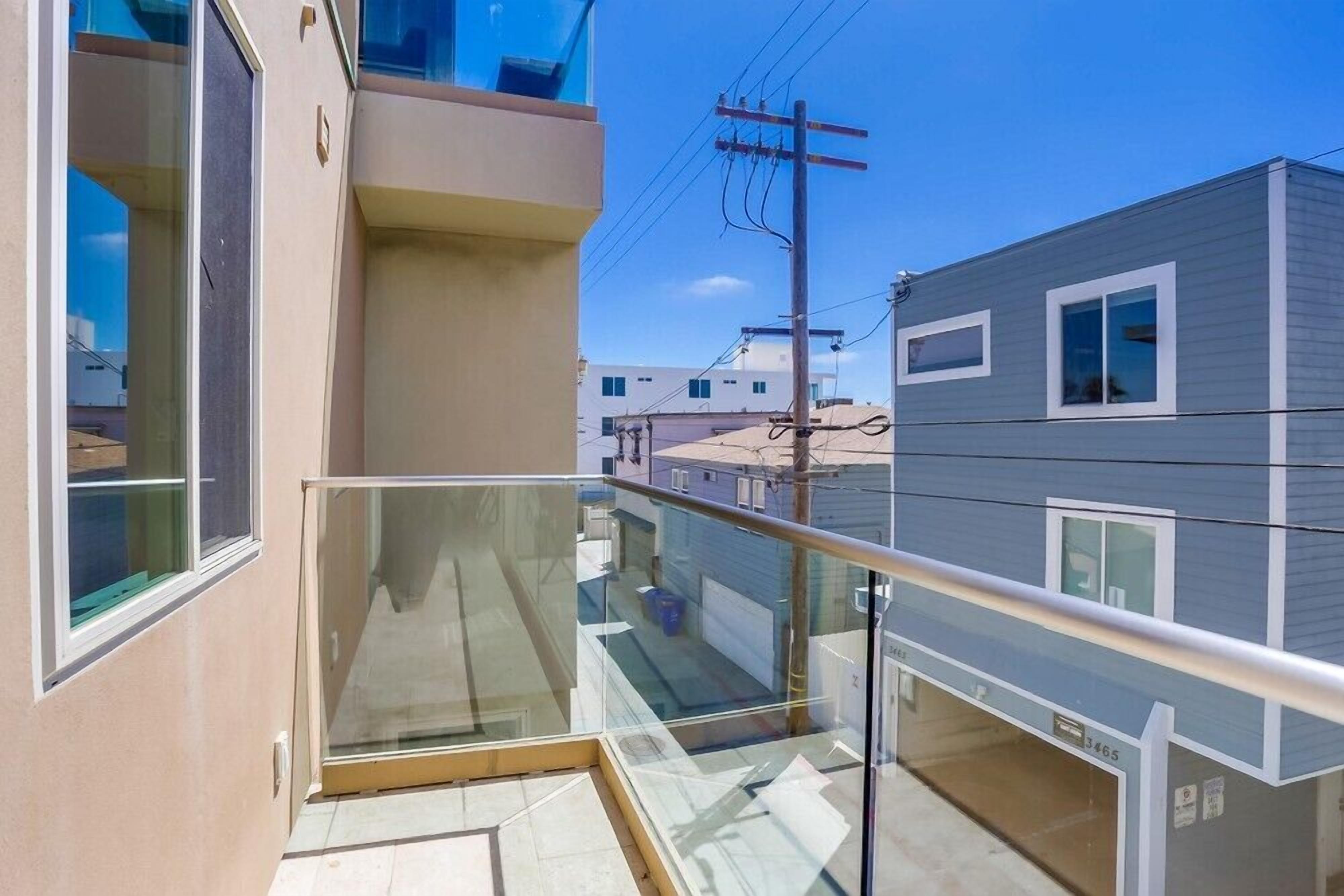 Un apartamento moderno con balcón de vidrio, vista a edificios vecinos y cielo despejado.