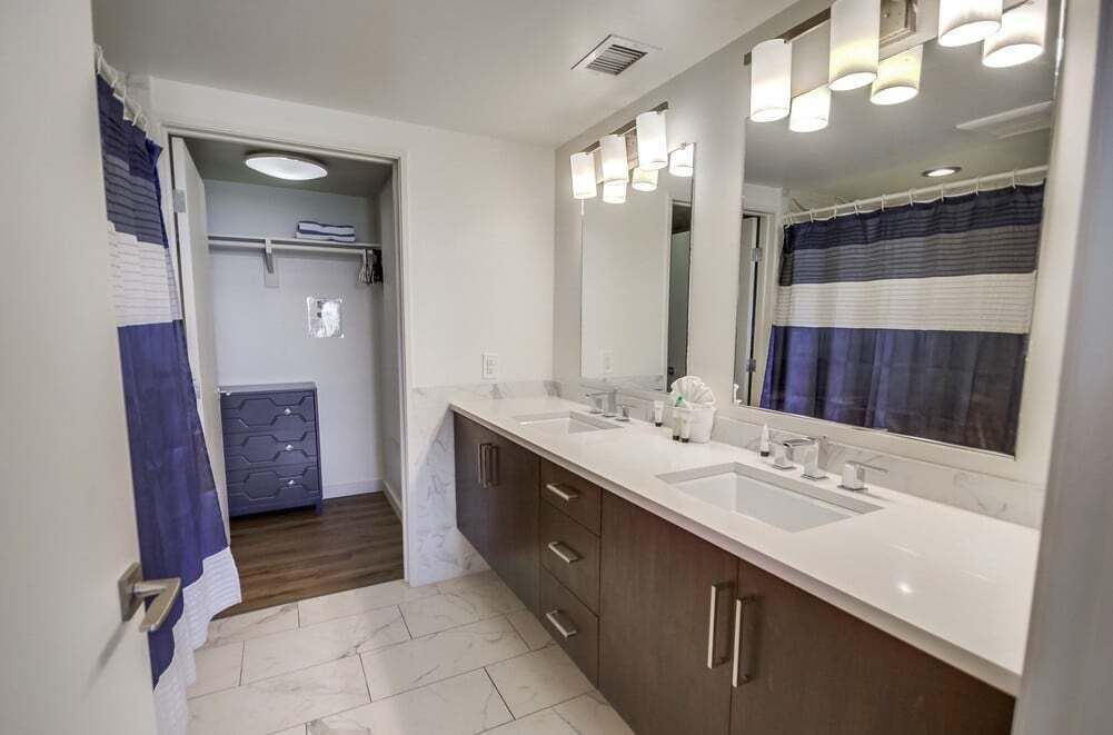 A modern bathroom with a double sink vanity, a large mirror, and a shower area.