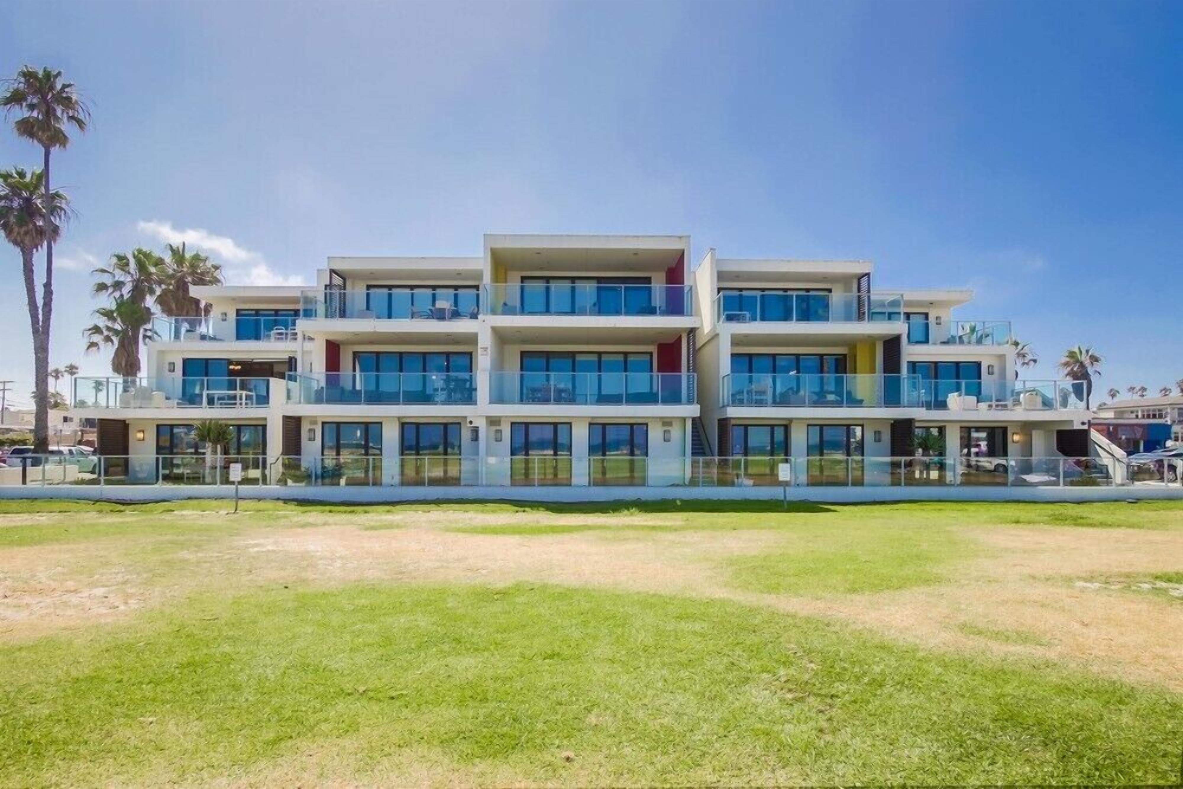 A multi-story hotel with balconies, large windows, and a grassy lawn in front.