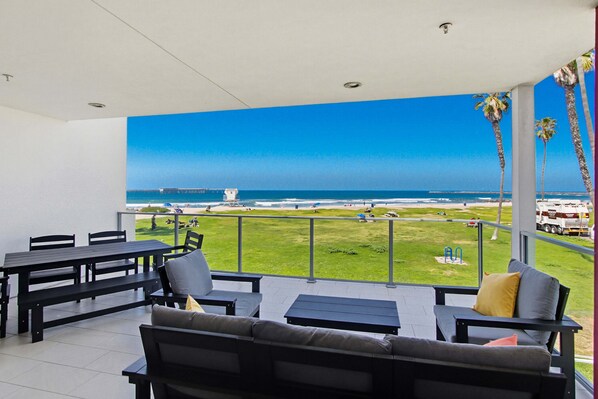 Un balcón con vista a la playa, mobiliario exterior y cielo despejado.