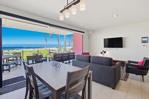 Una sala moderna con un televisor grande, un sofá gris y un comedor con mesa y sillas.