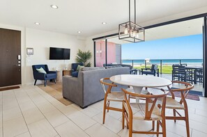 A modern living room with a sofa, chairs, a dining table, a TV, and a balcony with a view of the ocean. - Ocean Park 03 (San Diego)