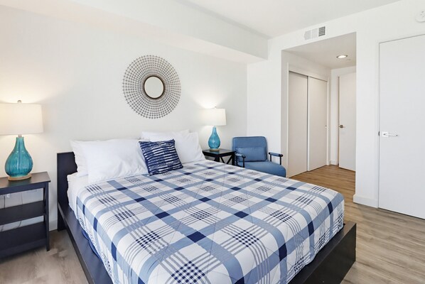 A bedroom with a large bed, a side table, a chair, a mirror, and a wardrobe. - Ocean Park 03 (San Diego)
