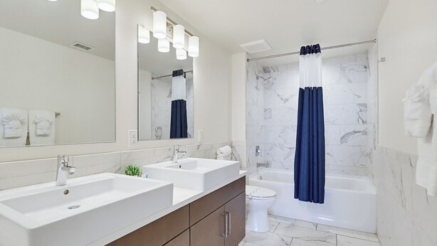 Une salle de bain avec un meuble-lavabo à deux vasques, des toilettes, une baignoire et un rideau de douche.