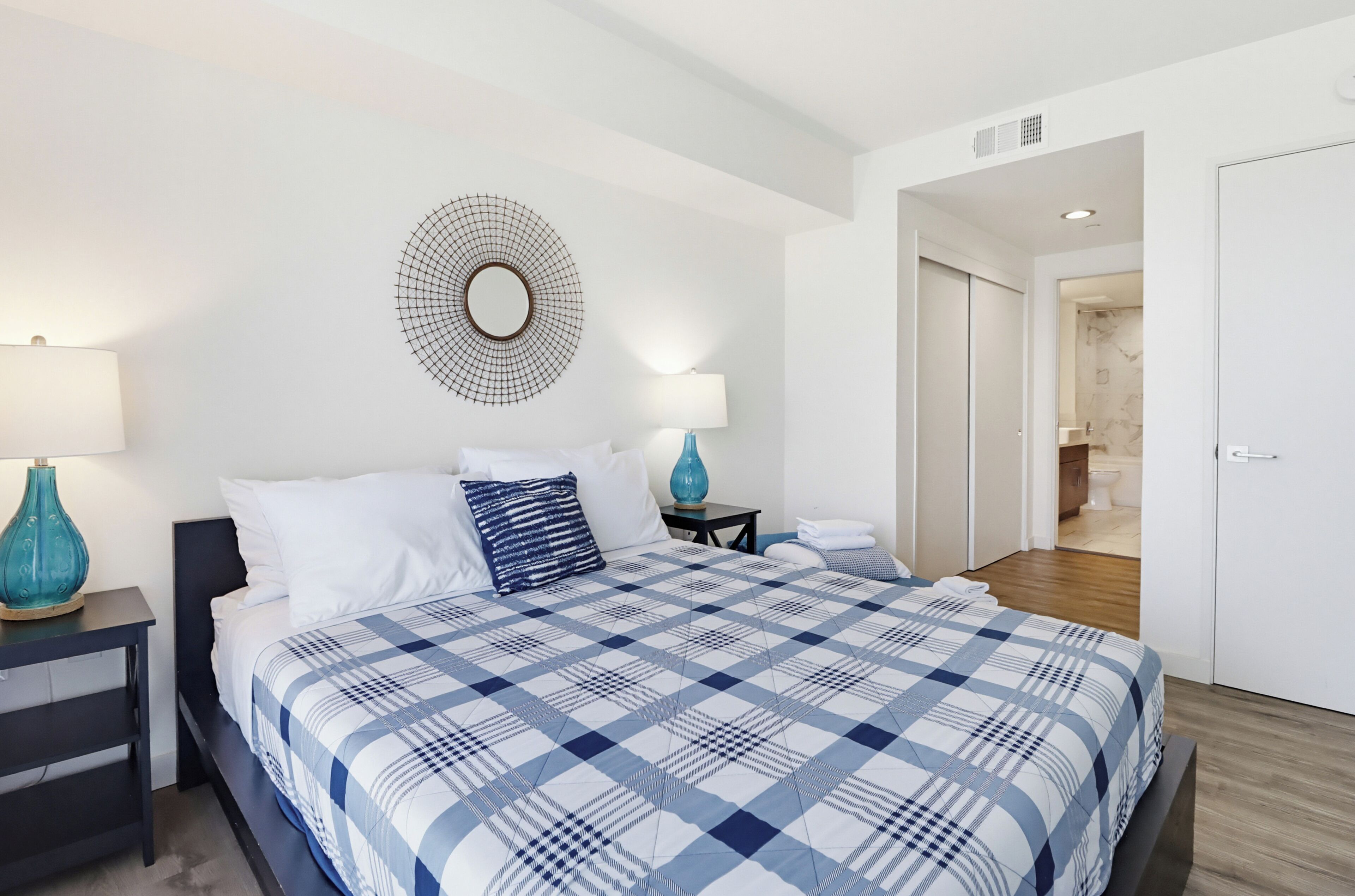 A hotel room with a large bed, two bedside tables, a wall-mounted mirror, and a bathroom visible through an open door.