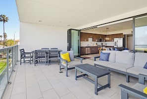 Un espacio exterior moderno con comedor, sofá y cocina visible a través de una puerta abierta.