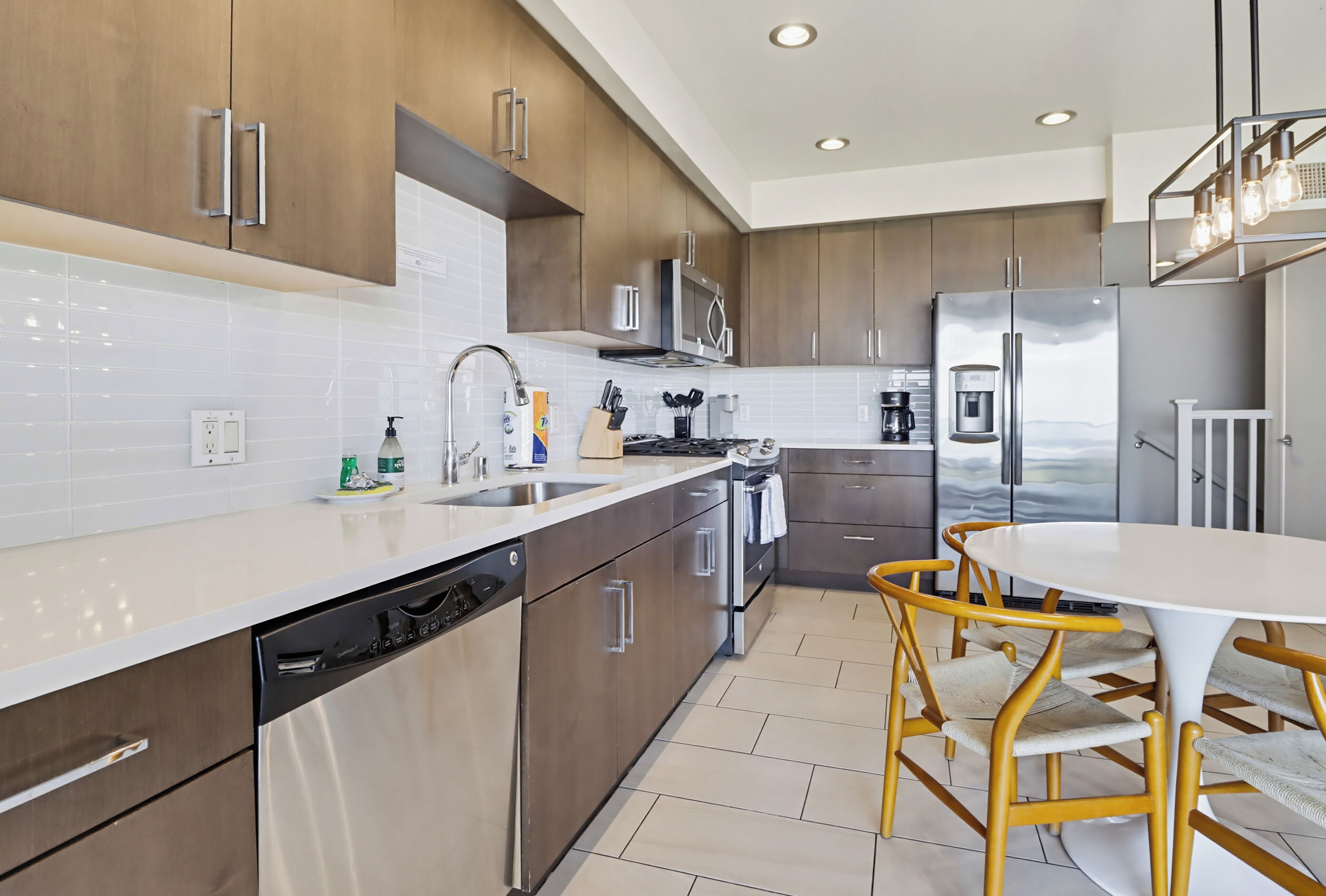 A modern kitchen with stainless steel appliances, wooden cabinets, and a white countertop.