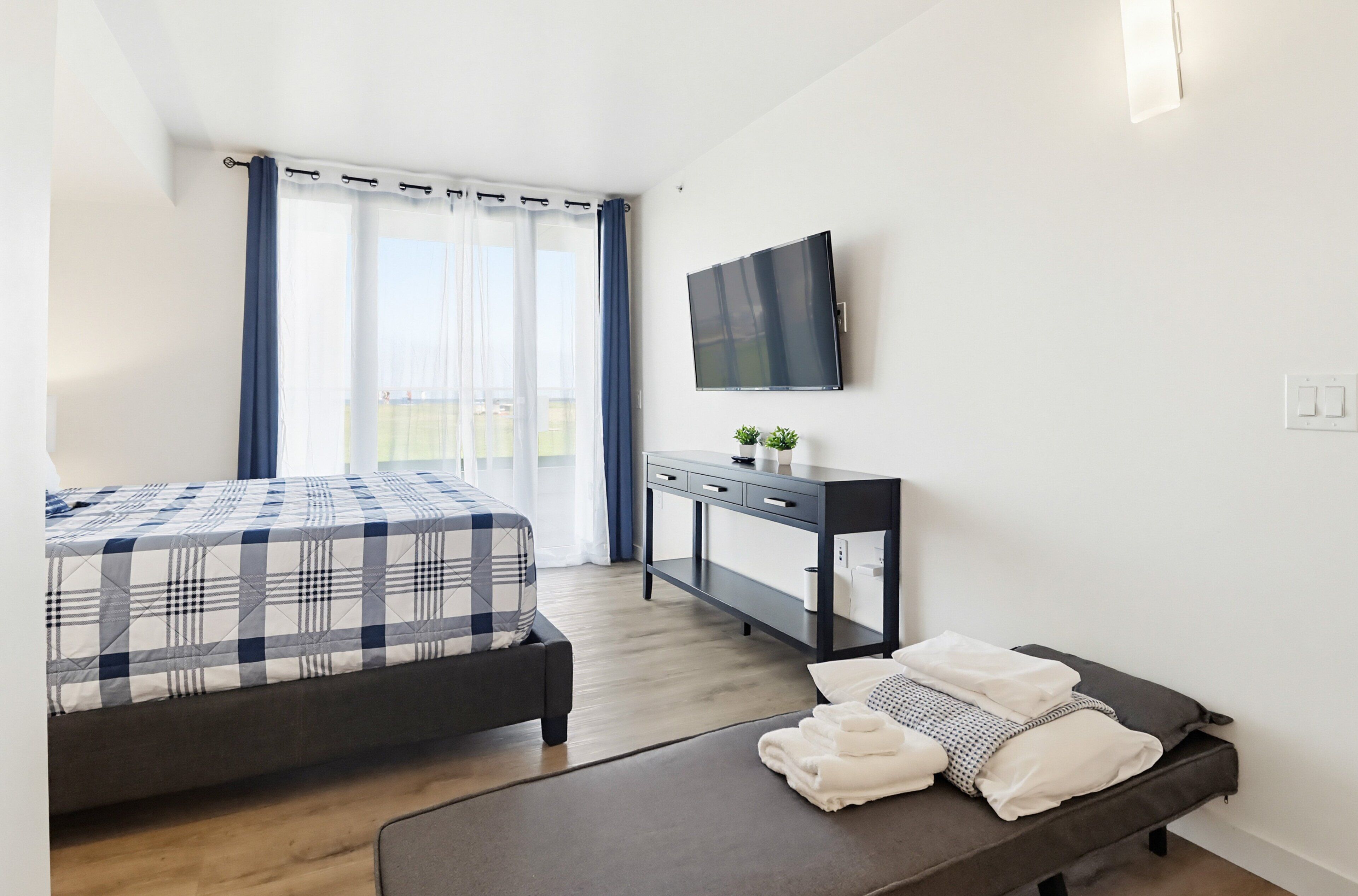 A modern hotel room with a bed, a desk, a TV, and a balcony view.