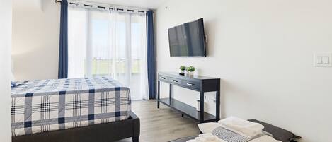 A modern hotel room with a bed, a desk, a TV, and a balcony view.