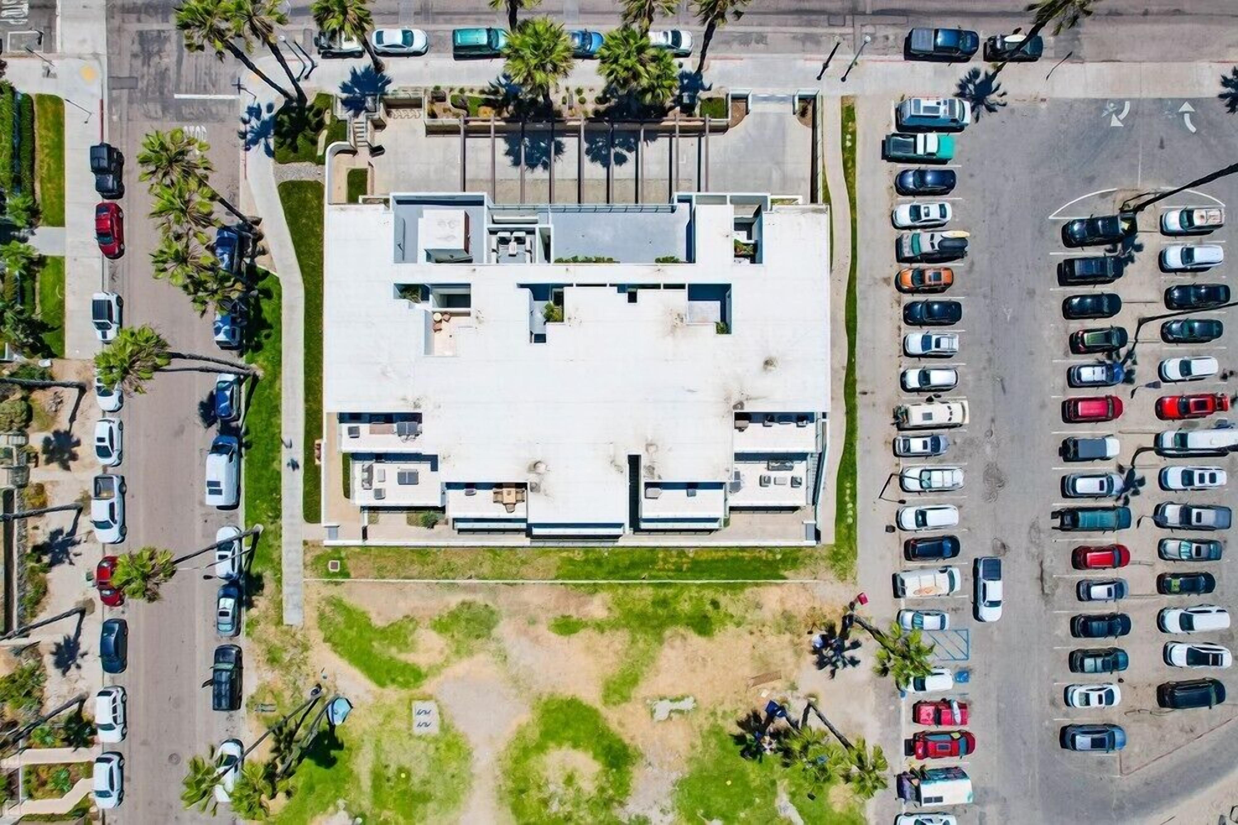 An aerial view of a parking lot with multiple rows of parked cars and a building with a flat roof in the center.