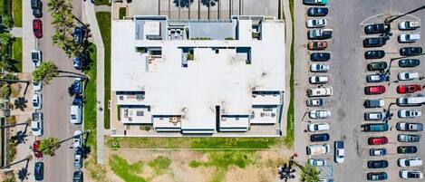 An aerial view of a parking lot with multiple rows of parked cars and a building with a flat roof in the center.