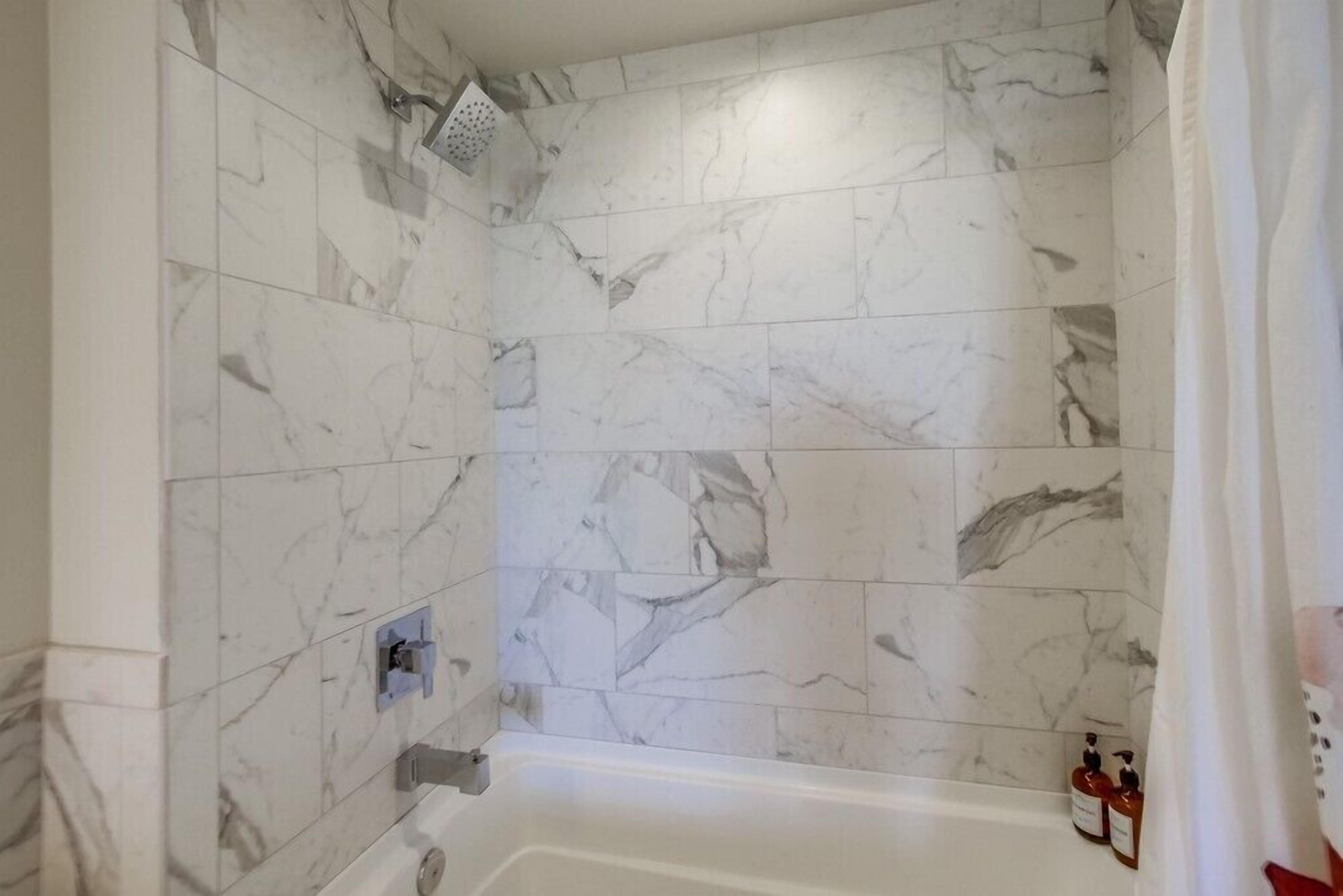Un baño con azulejos de mármol blanco, ducha y bañera.