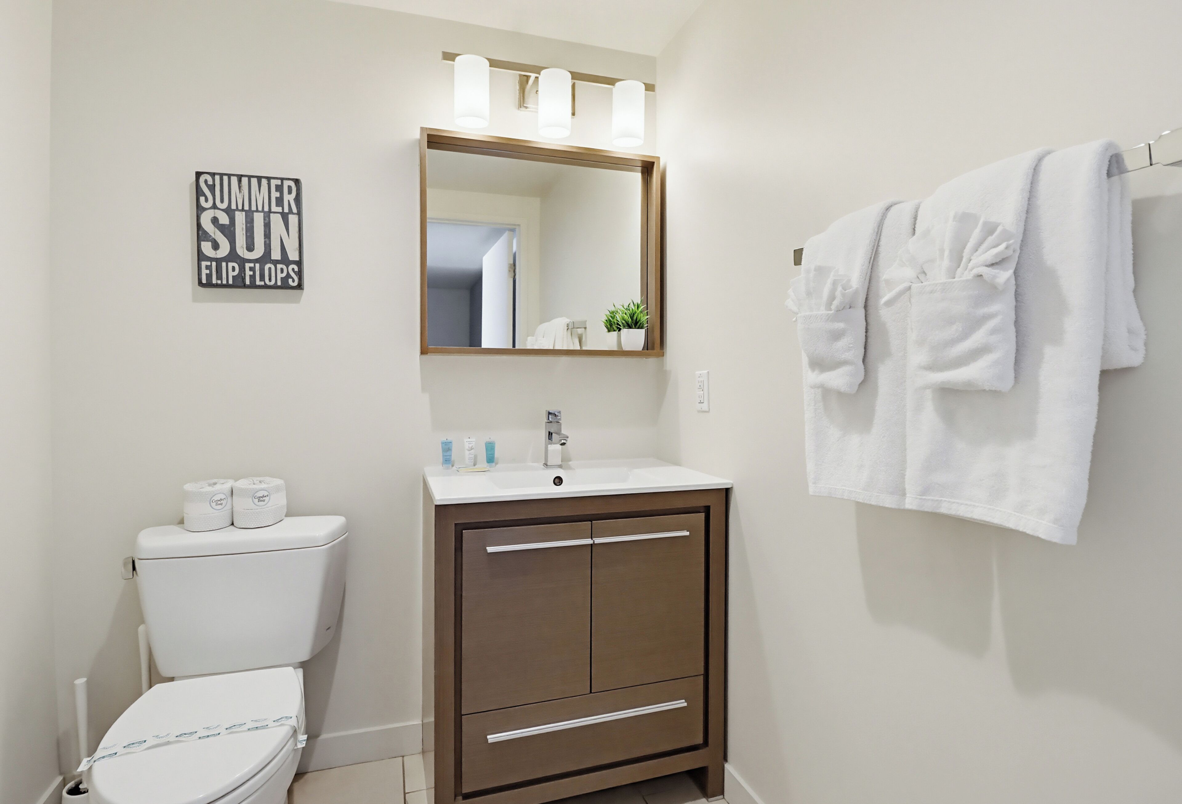 A bathroom with a toilet, sink, mirror, towel rack, and a sign on the wall.