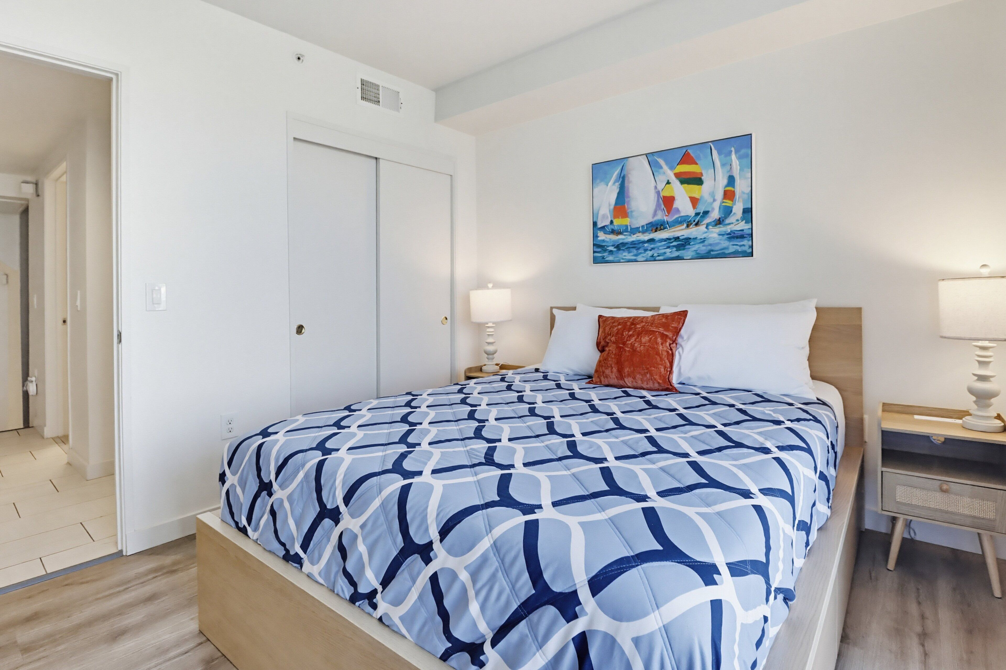 Un dormitorio con cama, mesita de noche, un cuadro y una puerta.
