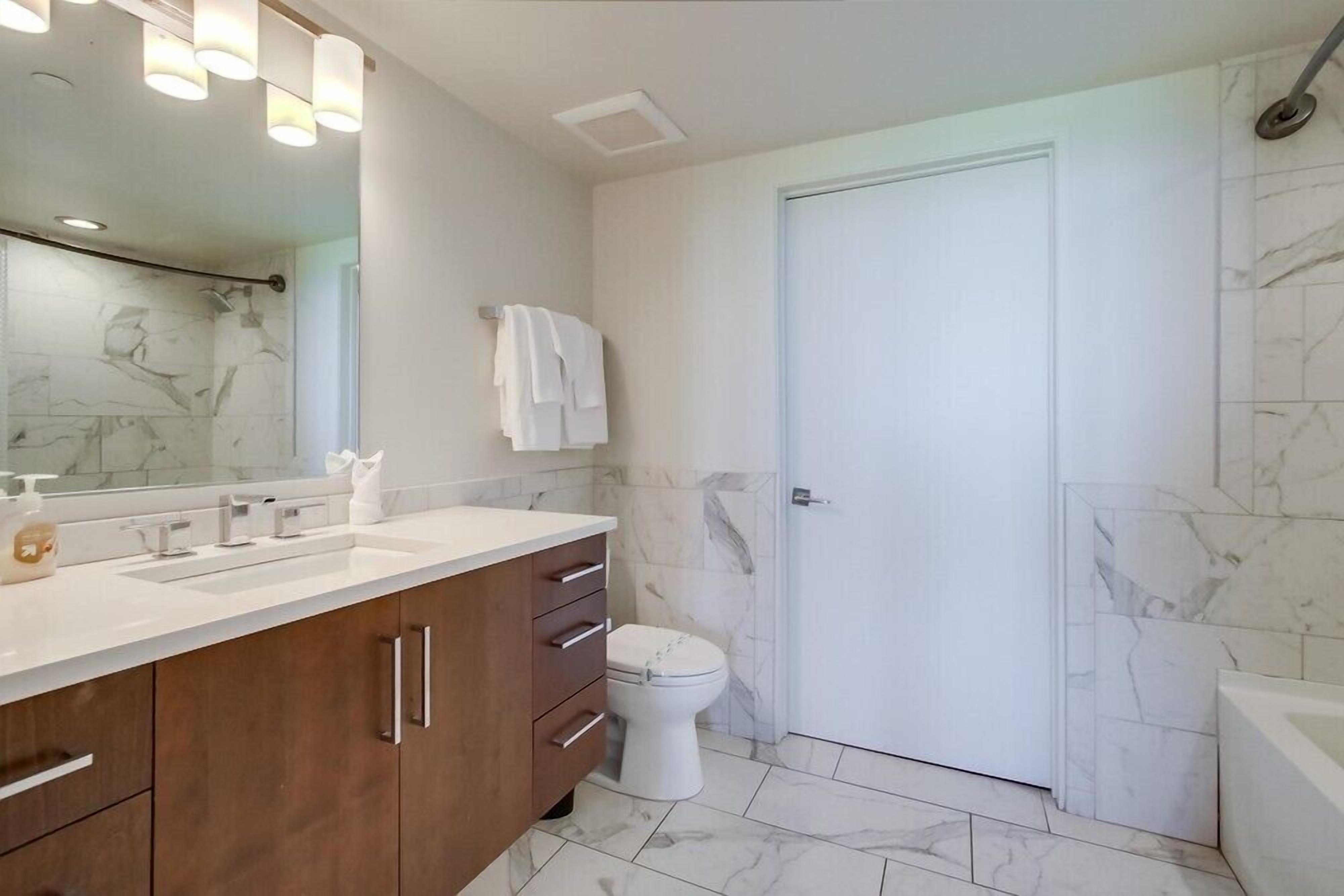 A modern bathroom with marble flooring, a large mirror, a double sink vanity, and a toilet.