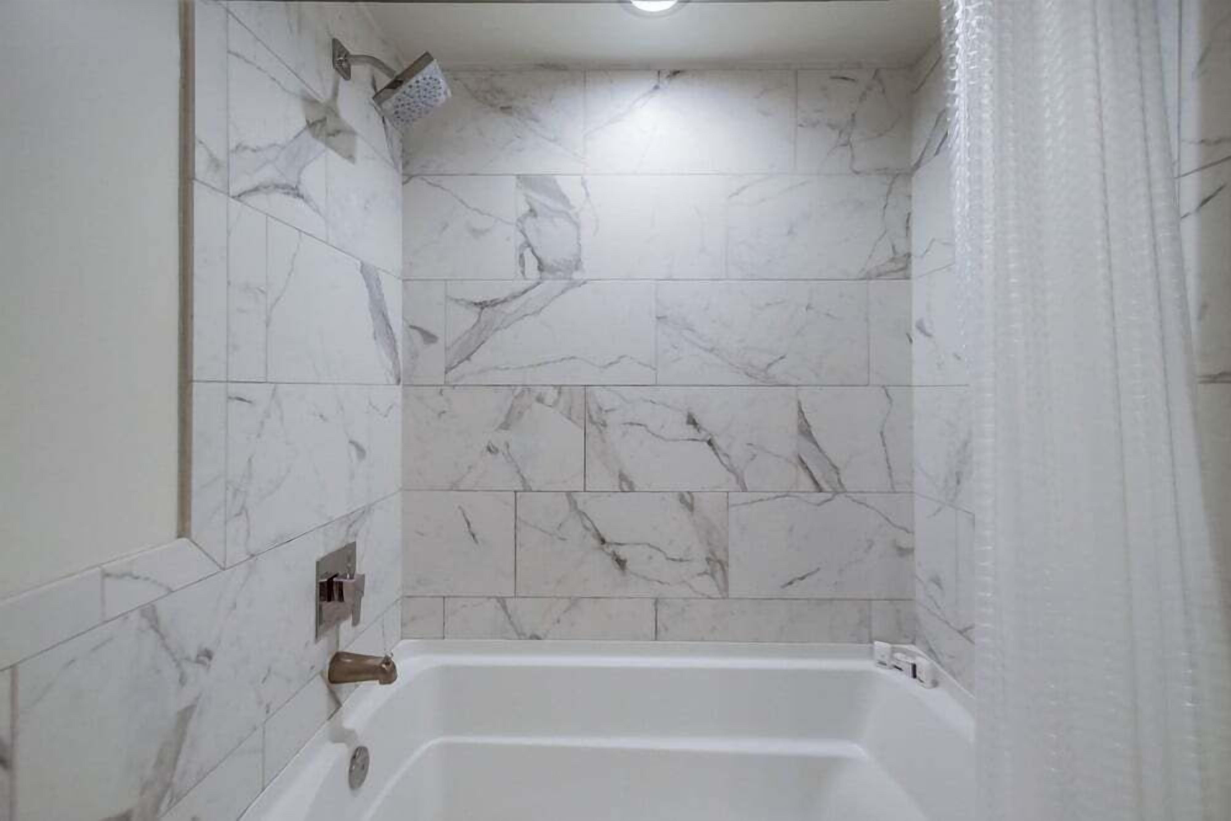 A bathroom with a bathtub, marble tiles, and a showerhead.