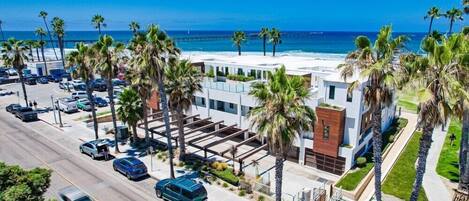 A modern hotel with a parking lot, palm trees, and a view of the ocean.