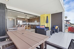 An outdoor patio area with a dining table, sofas, and a kitchen in the background.