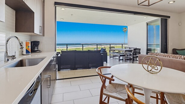 A modern kitchen with a large window, a dining area with a round table, and a view of the beach. - Ocean Park 04 (San Diego)