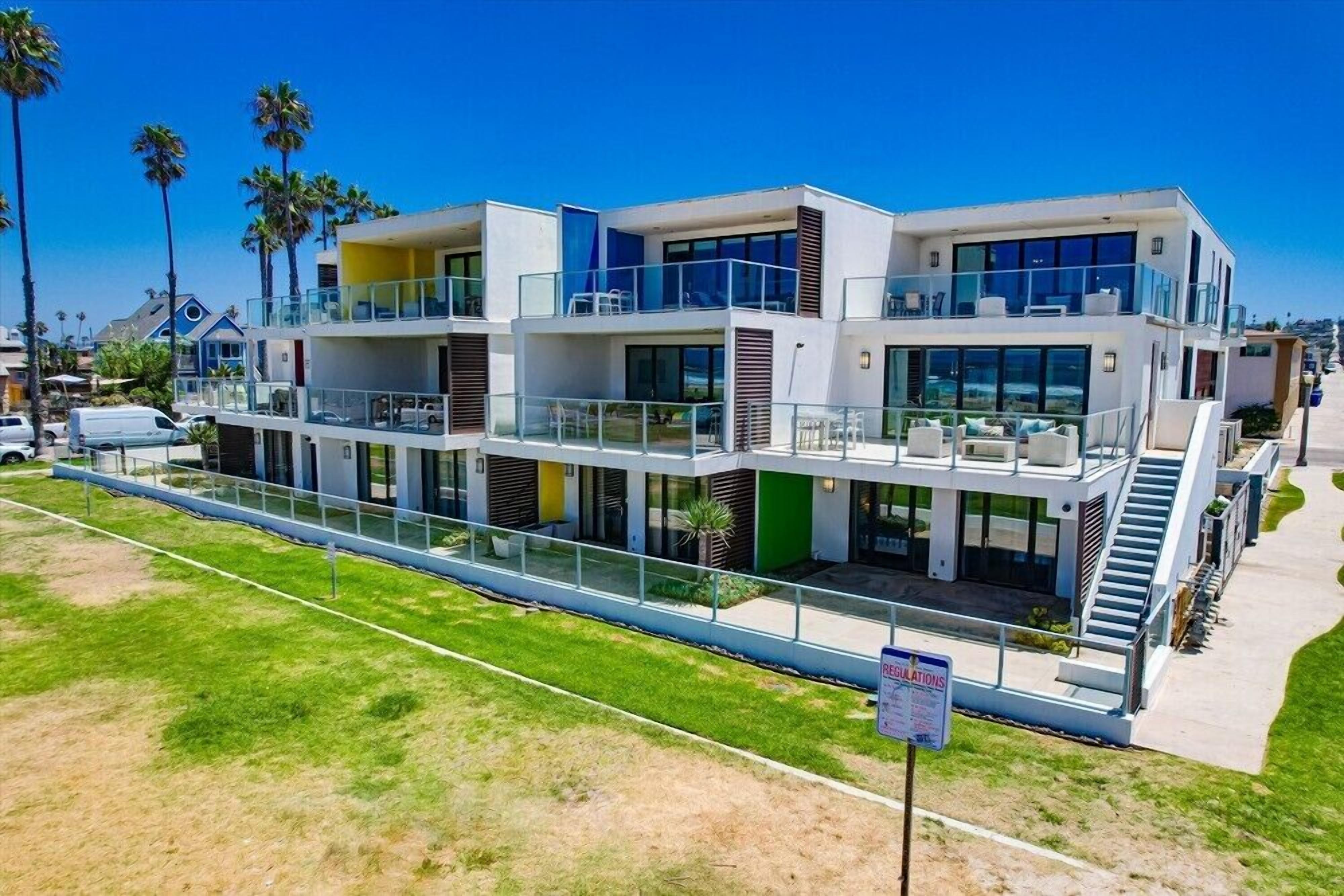 A modern multi-story building with balconies, a covered walkway, and a clear view of the surrounding area.