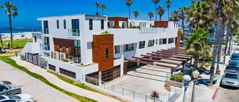 A modern multi-story building with a flat roof, large windows, and a parking area with cars.