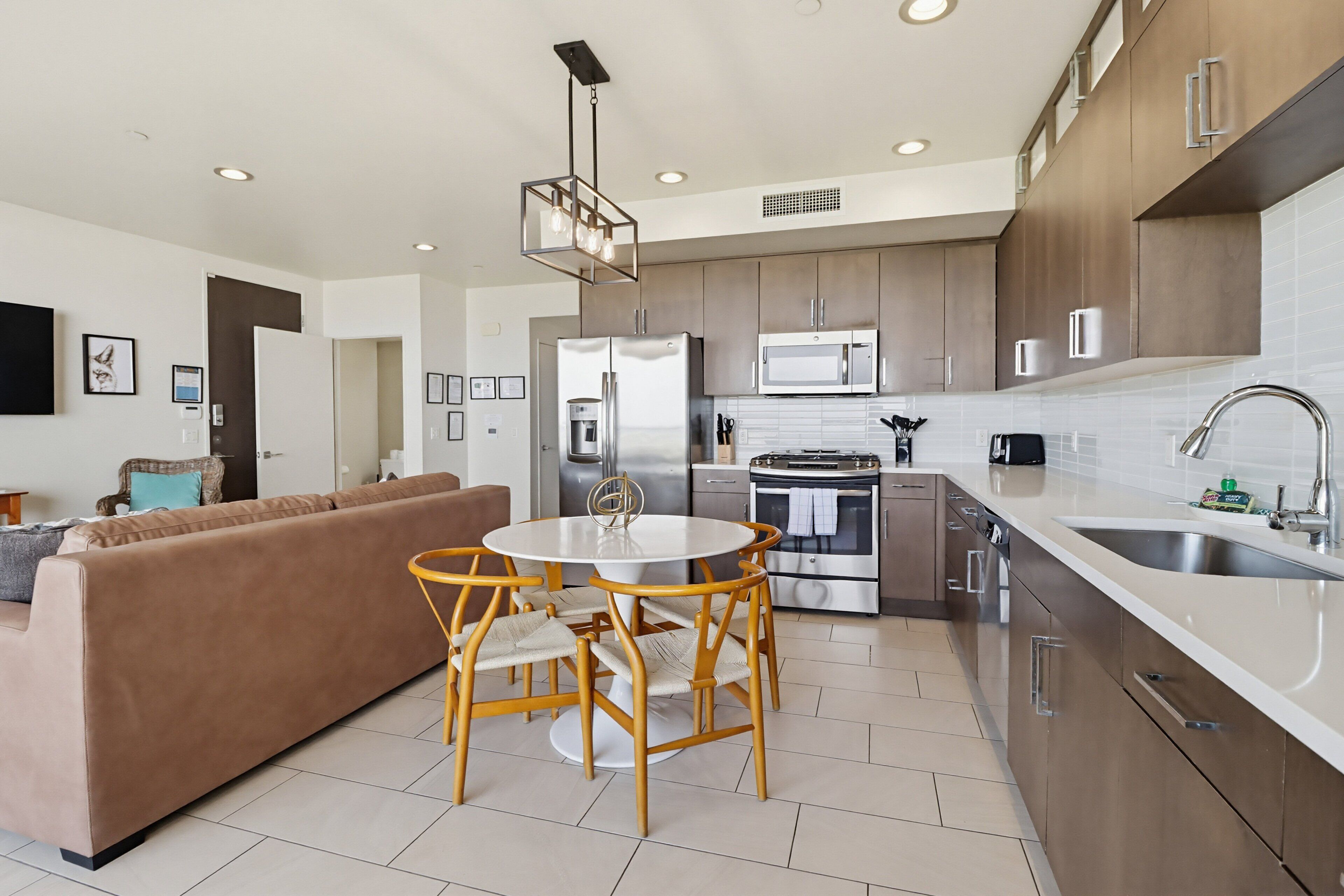 A modern kitchen with stainless steel appliances, a dining area with a round table and chairs, and a living room with a sofa.