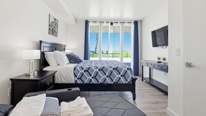 A modern bedroom with a bed, bedside table, TV, and a view of the outdoors. - Ocean Park 05 (San Diego)