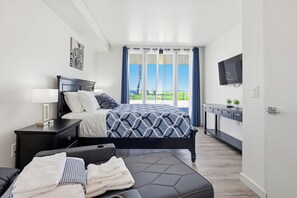 Un dormitorio moderno con cama, mesita de noche, televisor y vistas al exterior.