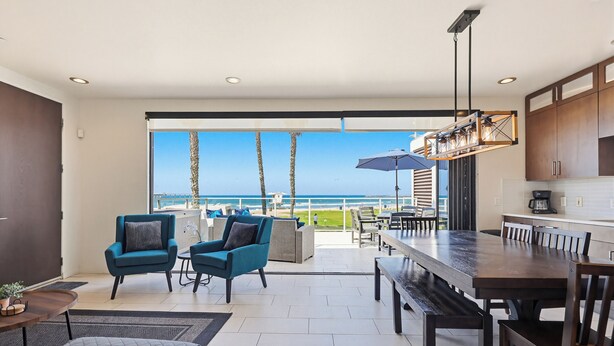 A modern kitchen with wooden cabinets, a dining area with a large table and chairs, and a view of the ocean through large sliding doors. - Ocean Park 05 (San Diego)