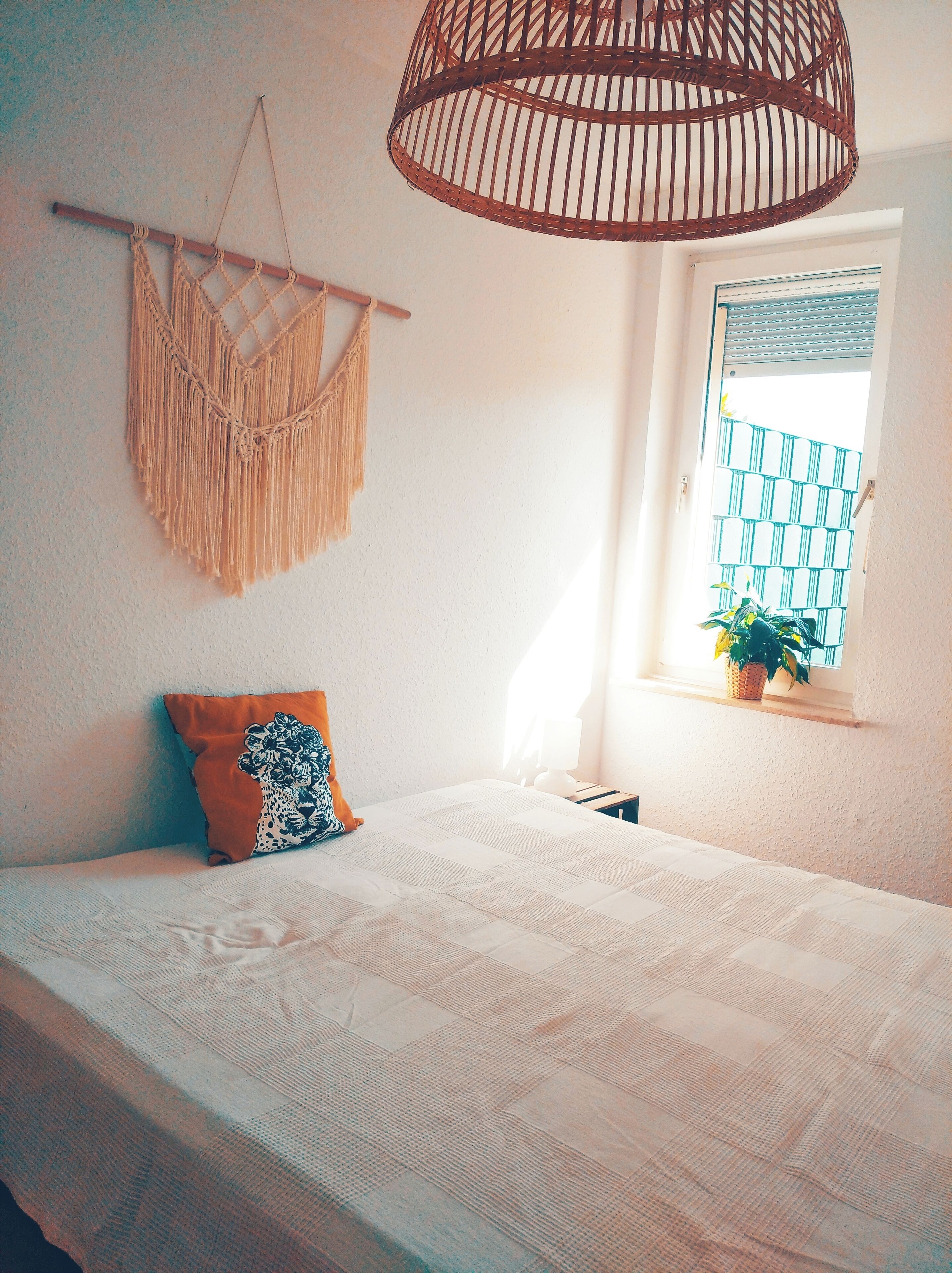 A bedroom with a bed, macrame wall hanging, and a hanging light fixture.