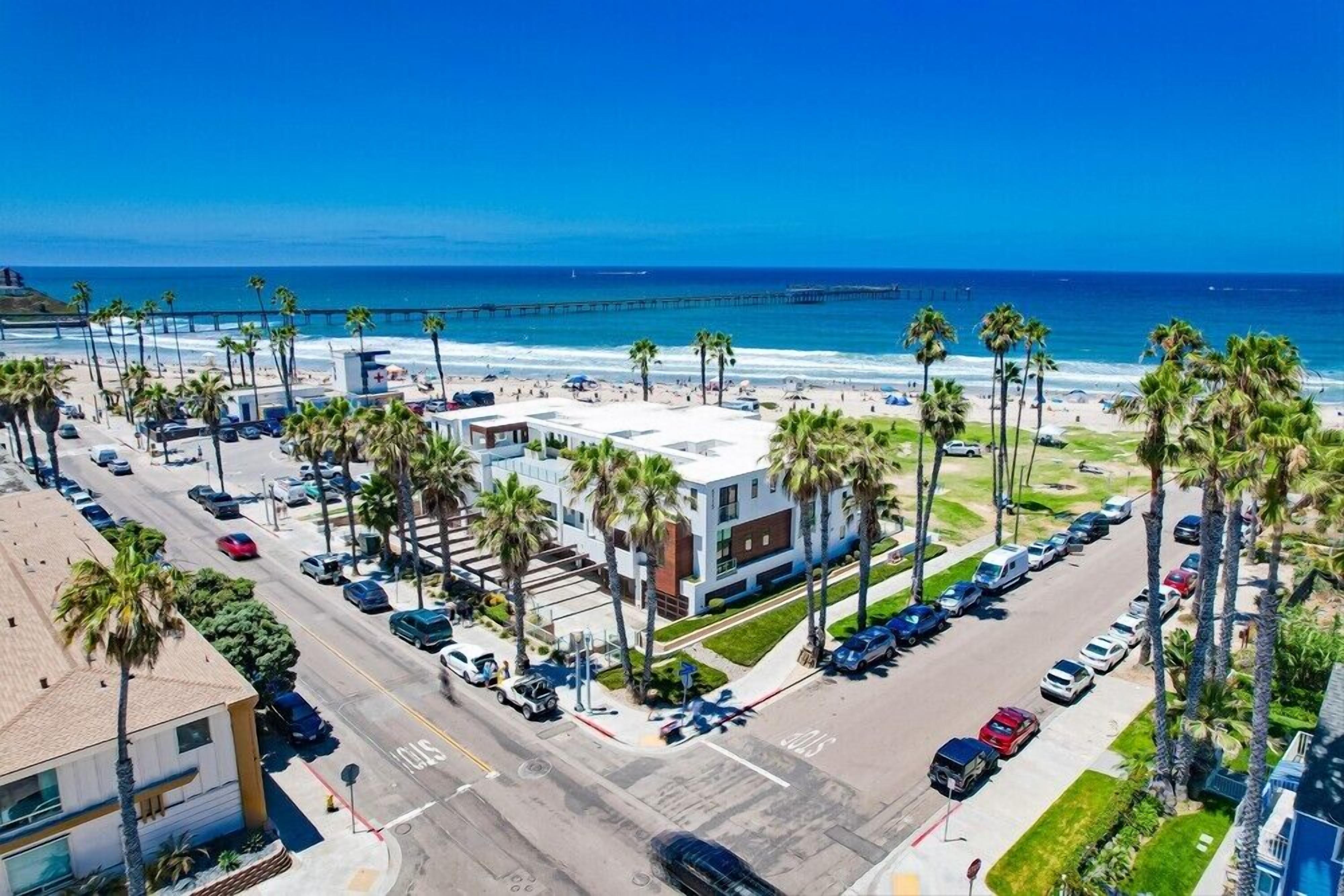 A coastal hotel with a parking lot, beach view, and palm trees.