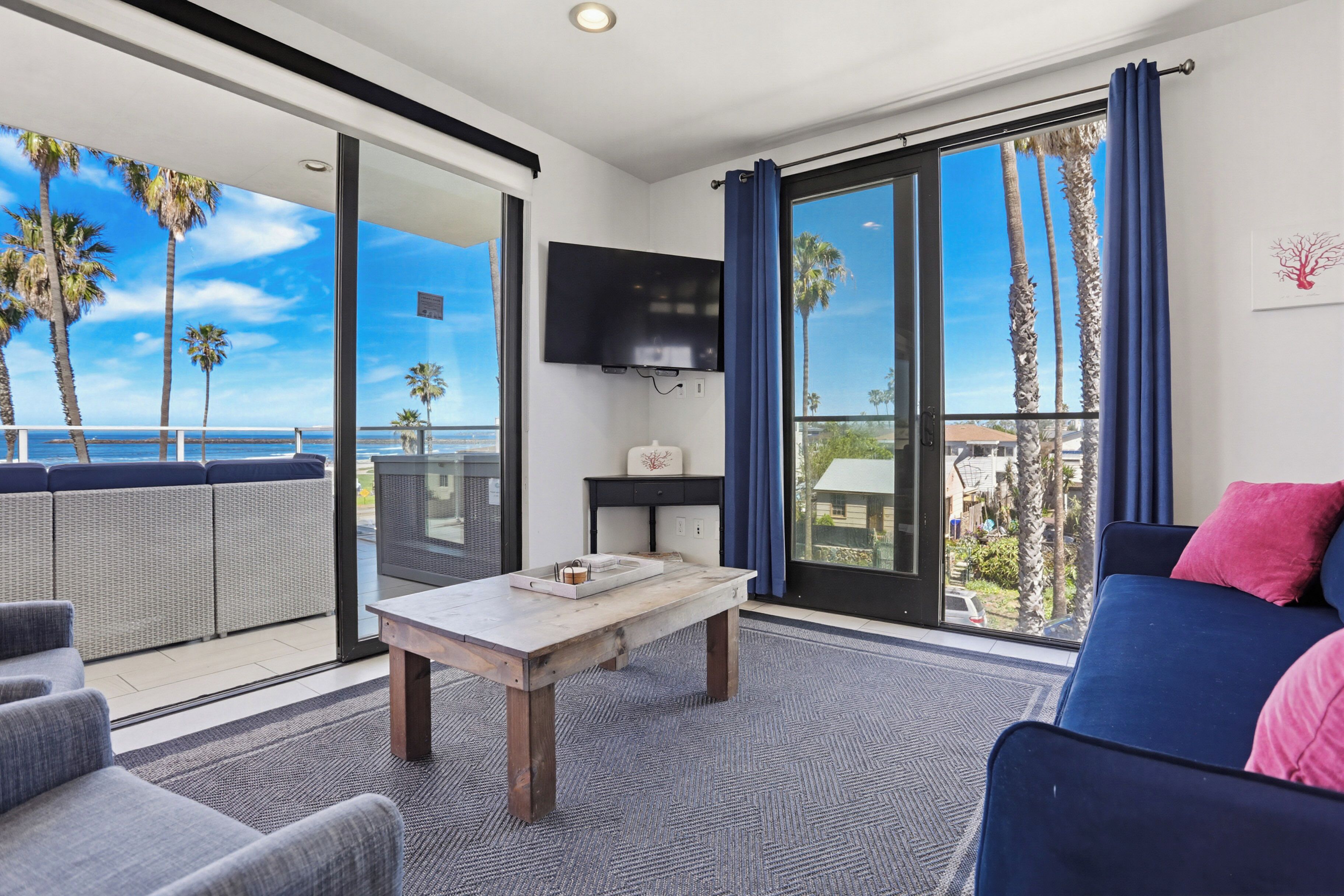 A room with a balcony, a TV, a table, and a sofa.
