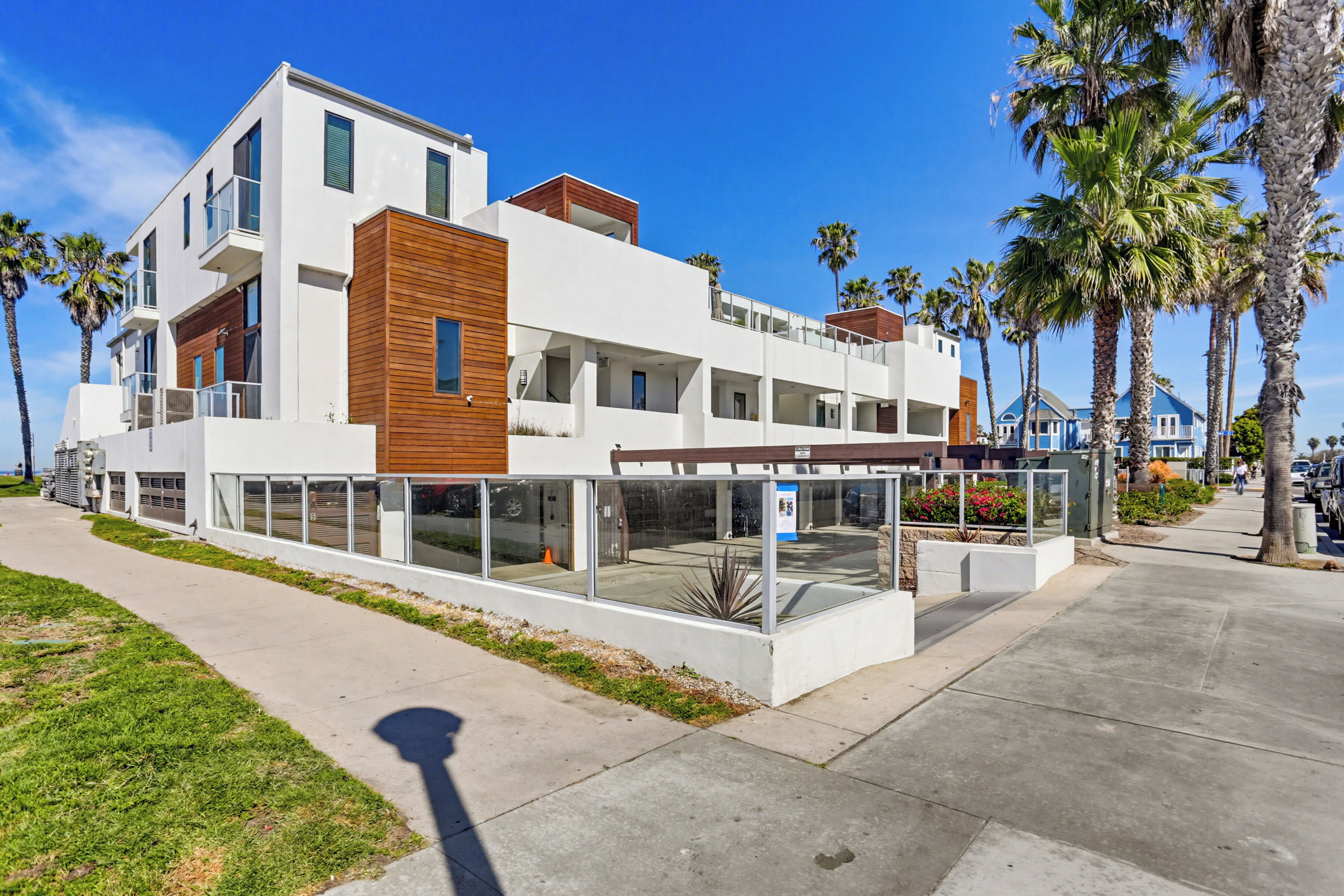 A modern multi-story building with balconies, a glass facade, and a landscaped area with palm trees.