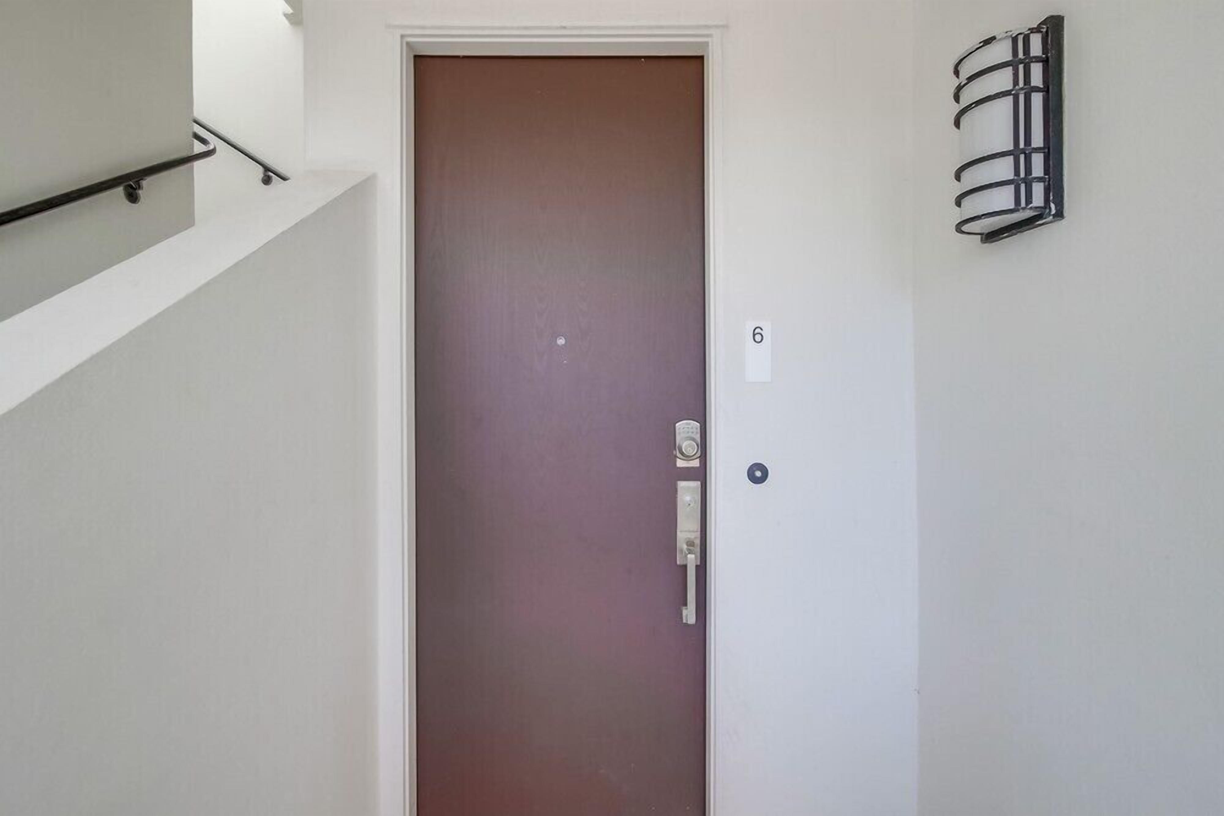 Une porte fermée avec une plaque portant le numéro 6, une main courante en métal et un luminaire fixé au mur.