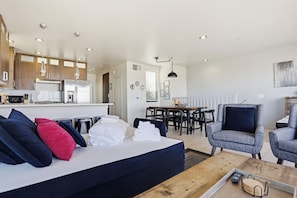 A modern hotel room with a sofa, chairs, a dining table, a kitchen area, and a large window. - Ocean Park 06 (San Diego)
