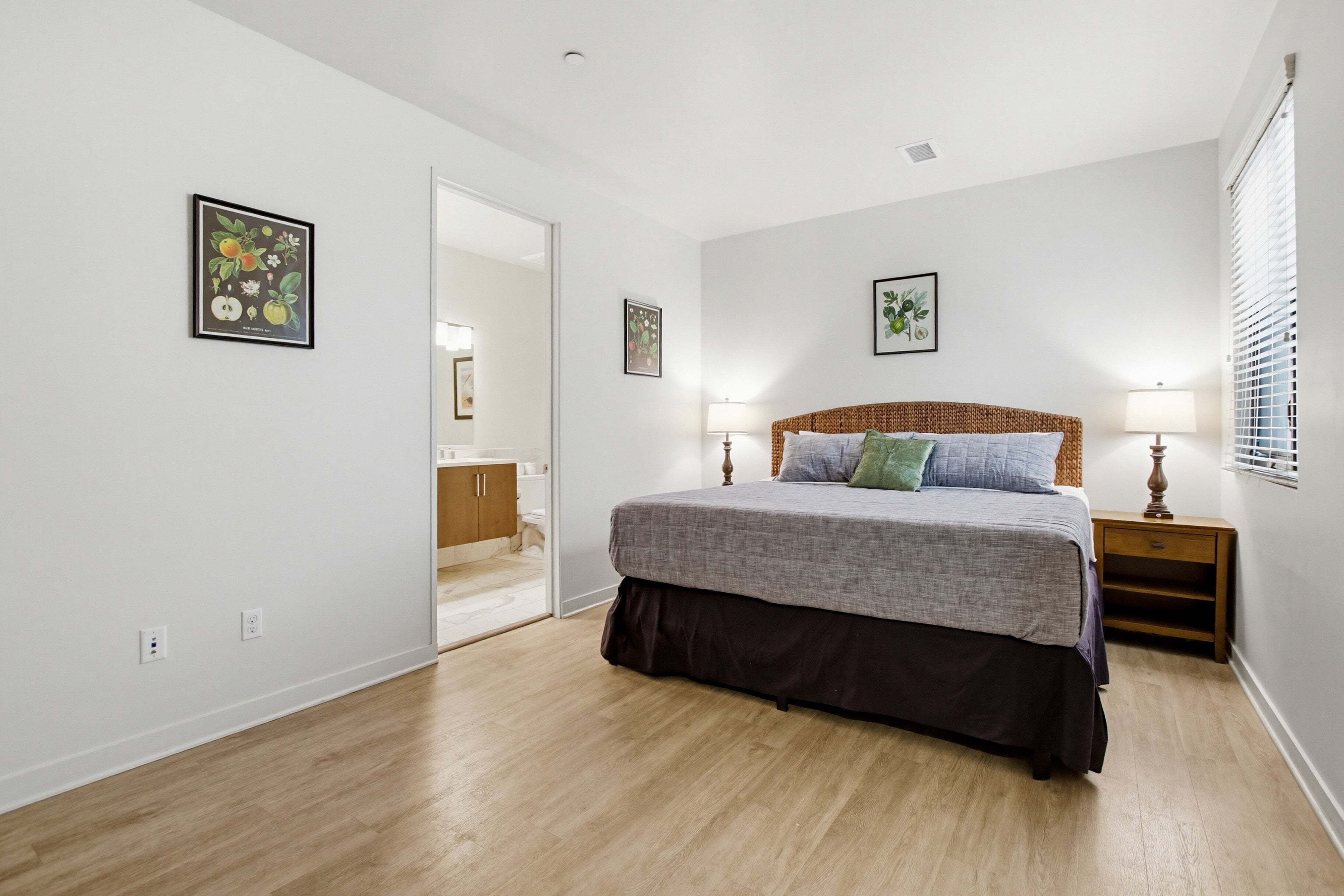Un dormitorio con cama, lámparas de noche, una puerta que da a otra habitación y una obra de arte colgada en la pared.