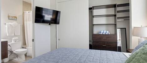 A bedroom with a bed, a TV, a wardrobe, a mirror, and a bathroom with a toilet and shower curtain.