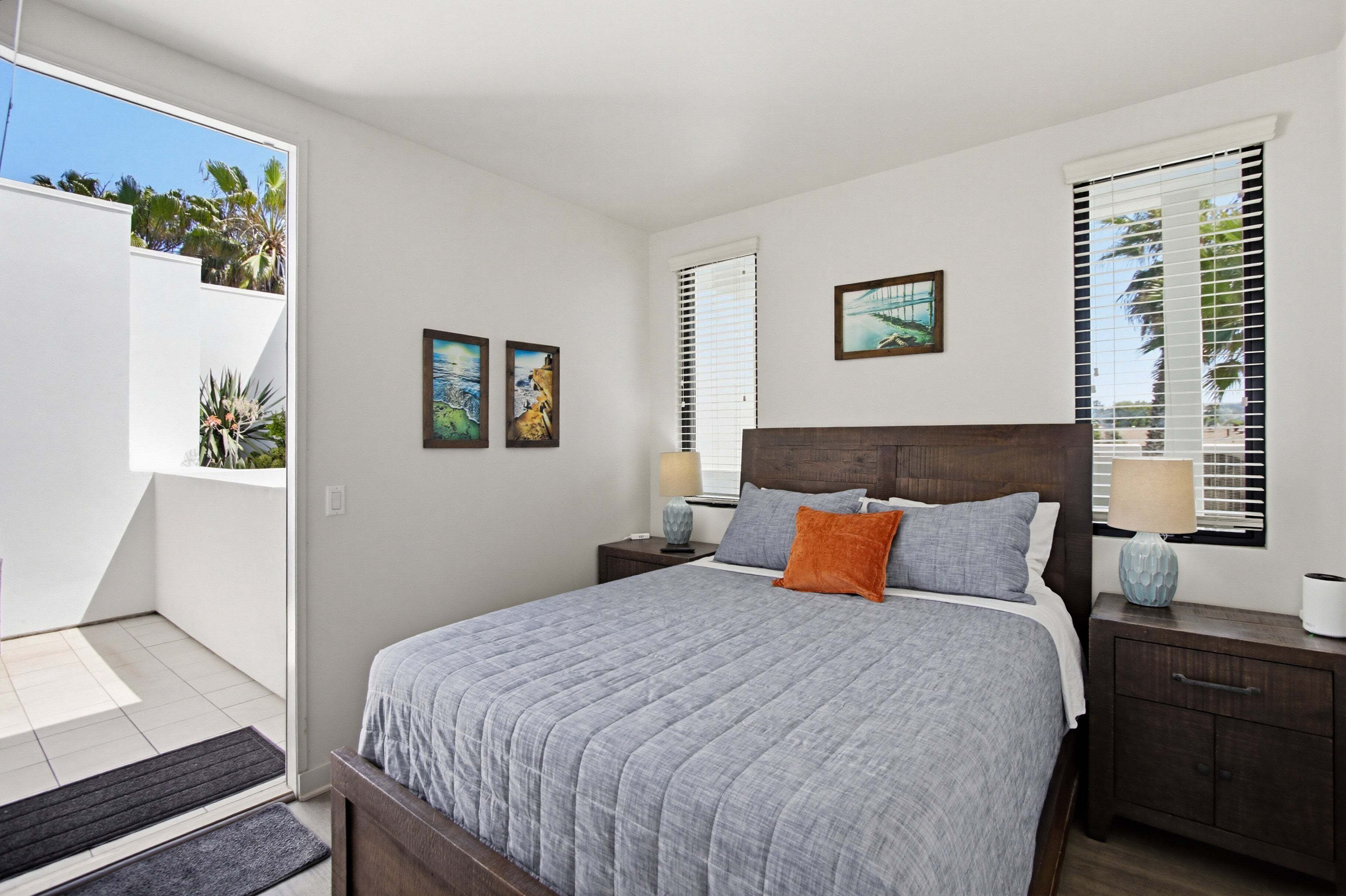 A bedroom with a bed, nightstands, a window with blinds, and artwork on the wall.