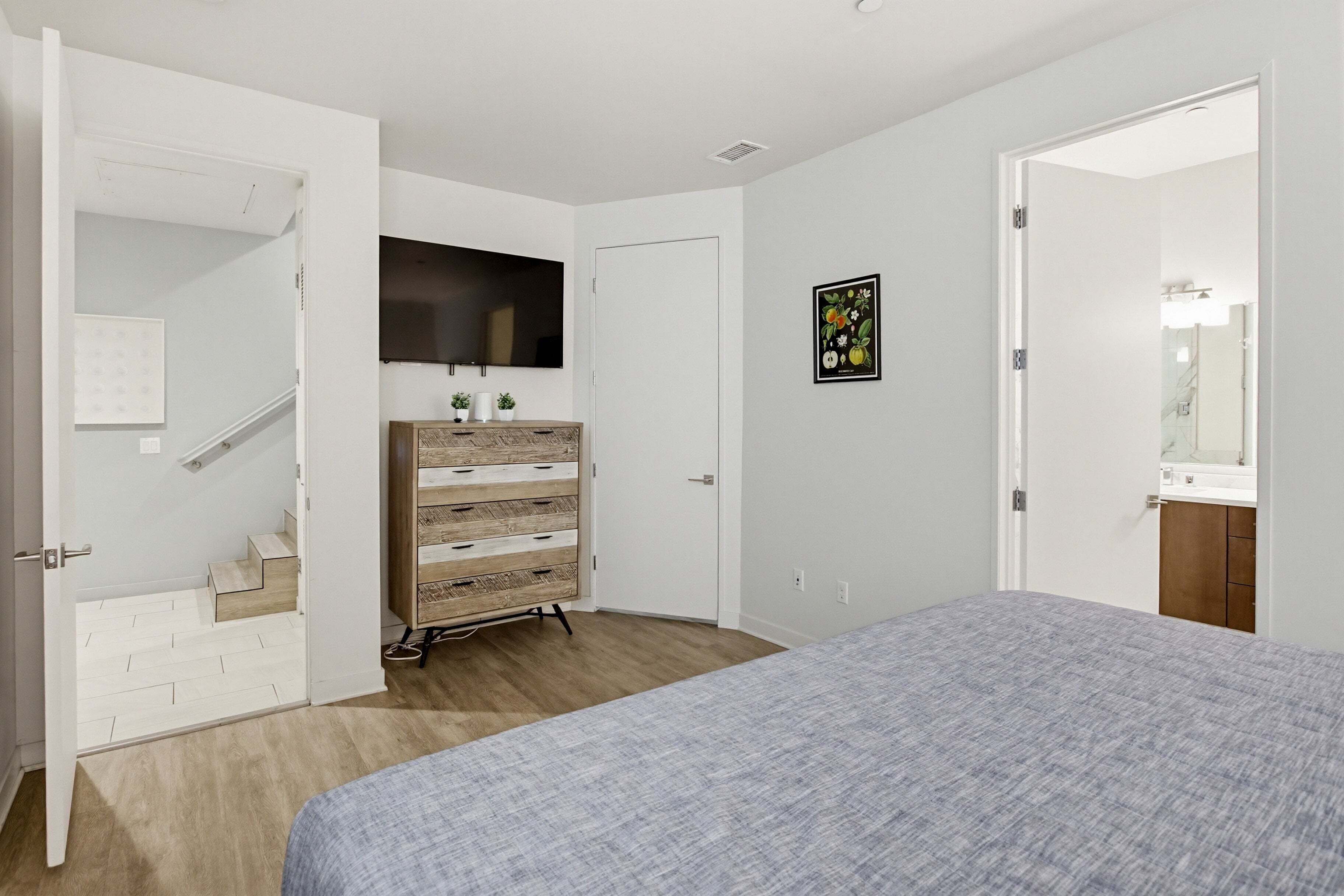 Un dormitorio con cama, cómoda, televisor y puerta que da a un baño.