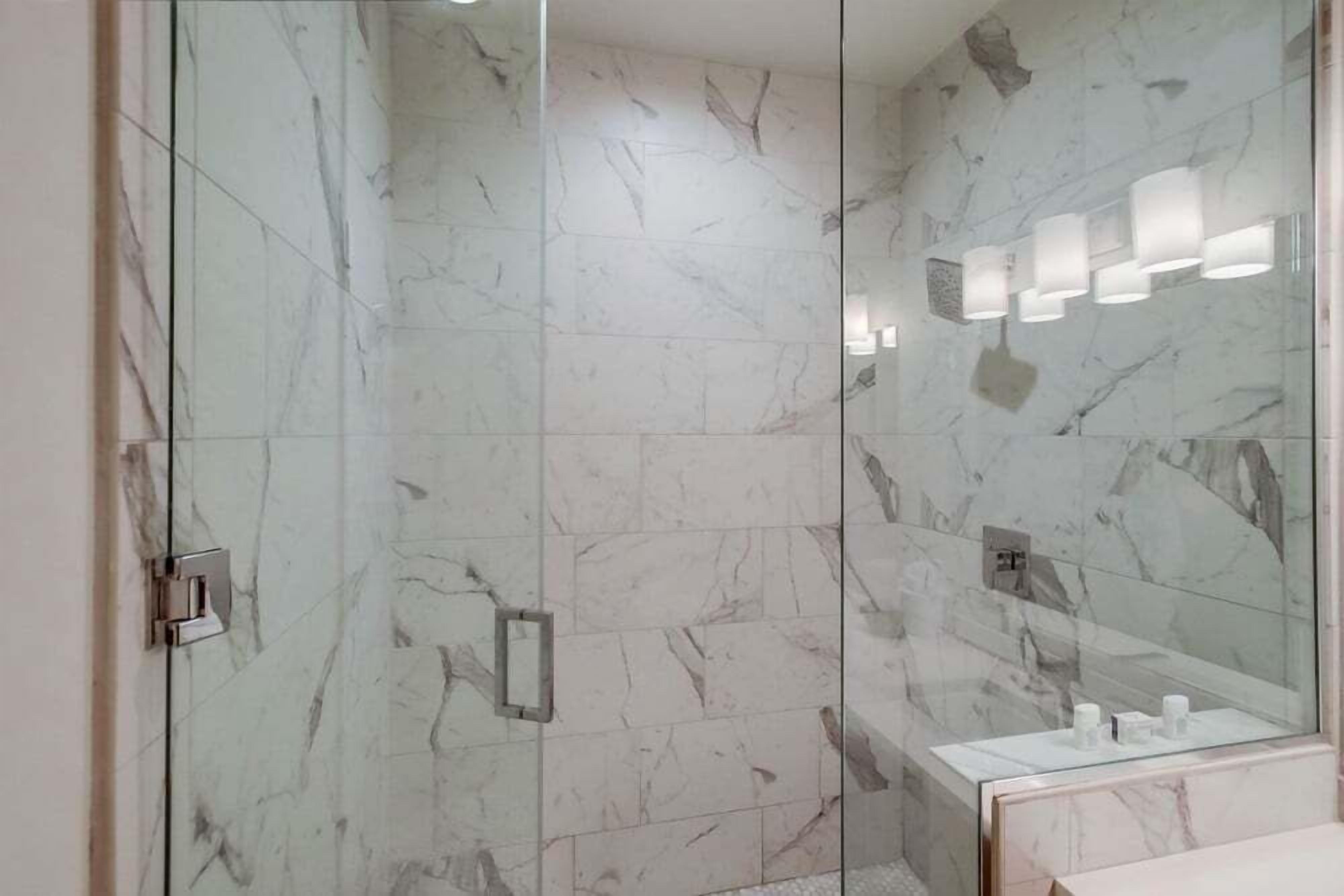 Un baño moderno con paredes de mármol, cabina de ducha de vidrio y tocador con espejo.