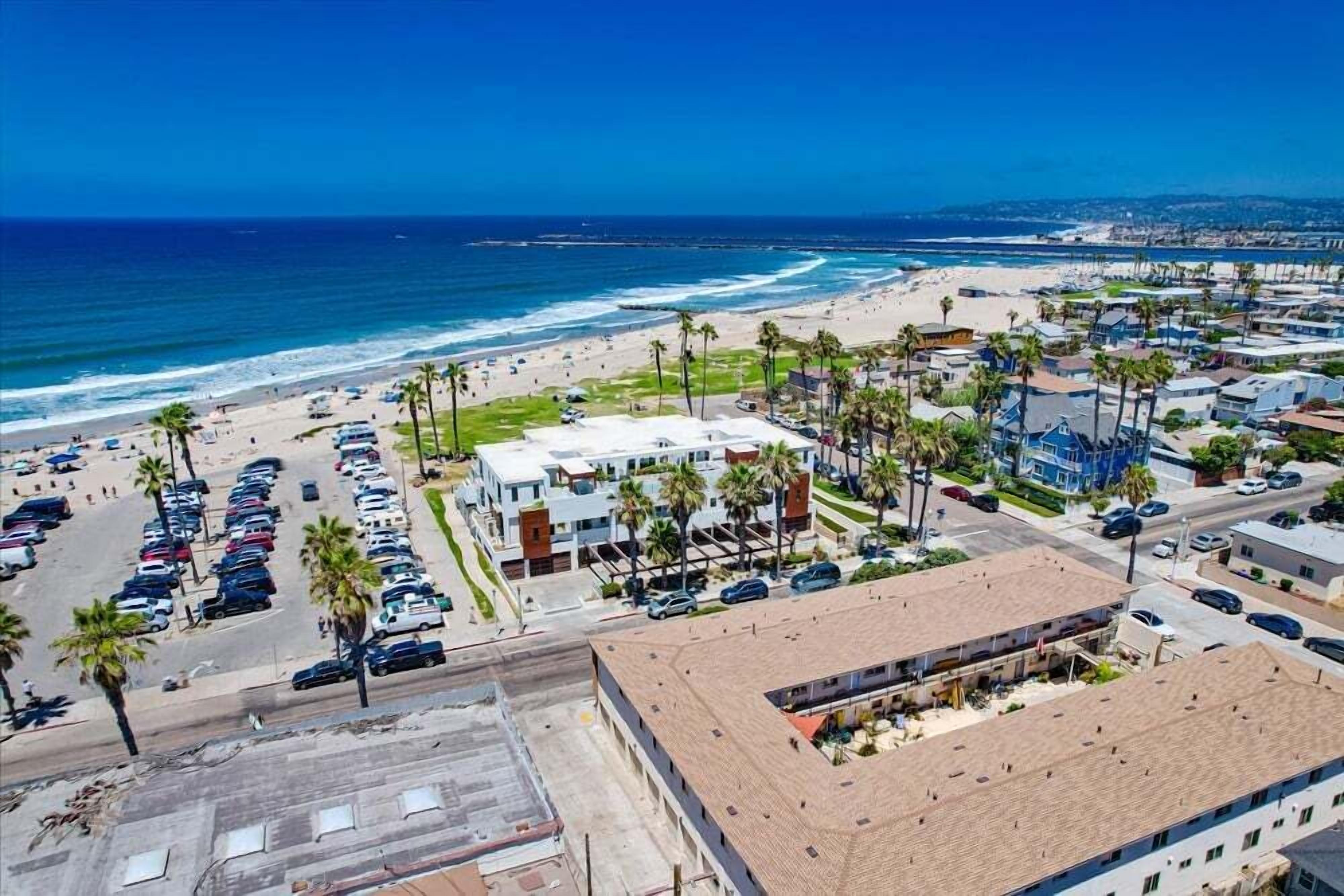 A coastal area with a beach, parking lots, and buildings with flat roofs.