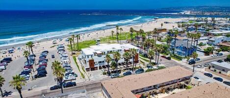 A coastal area with a beach, parking lots, and buildings with flat roofs.