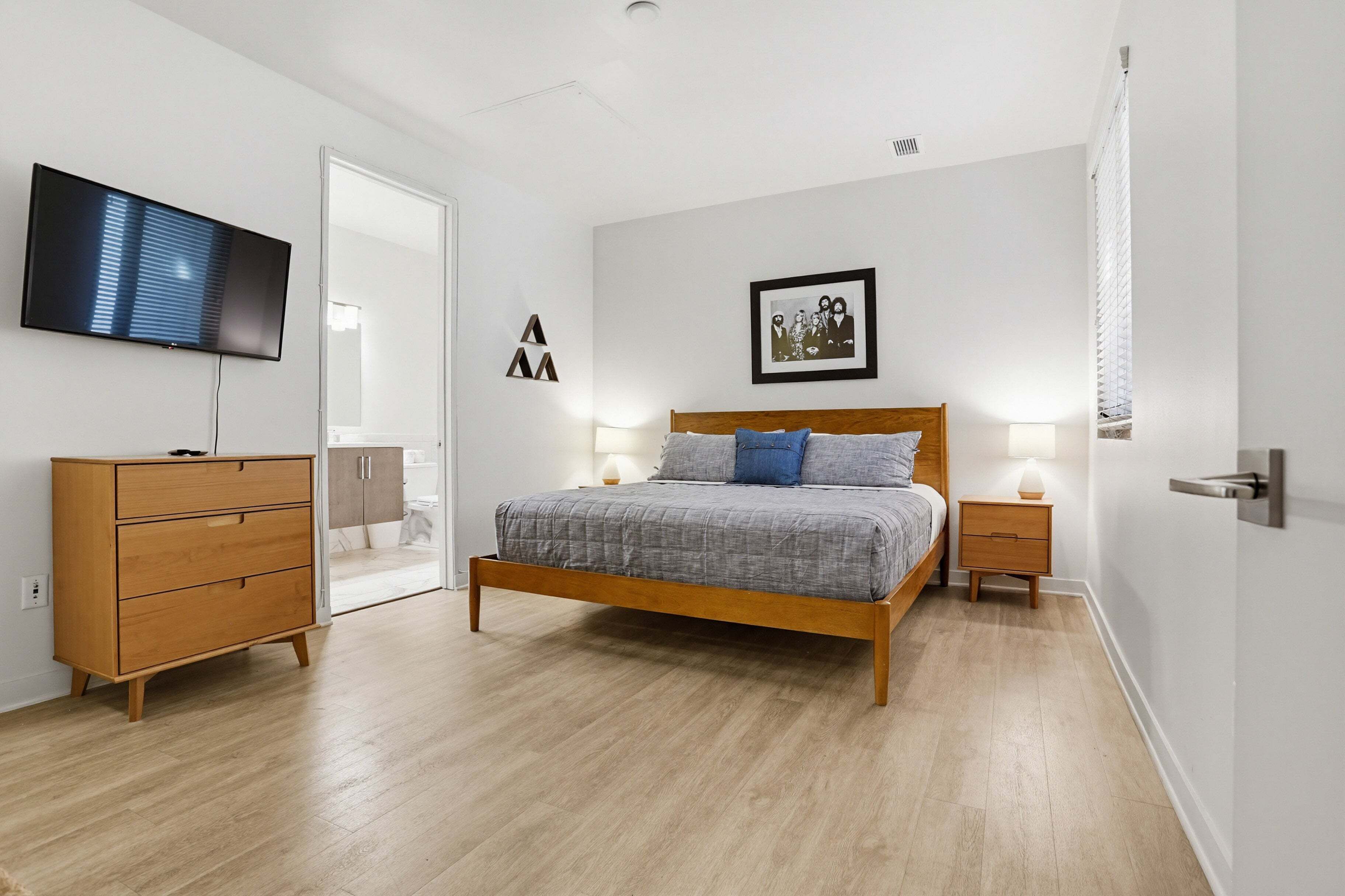 A bedroom with a bed, dresser, TV, and framed picture on the wall.