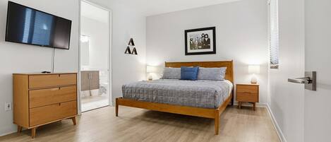A bedroom with a bed, dresser, TV, and framed picture on the wall.