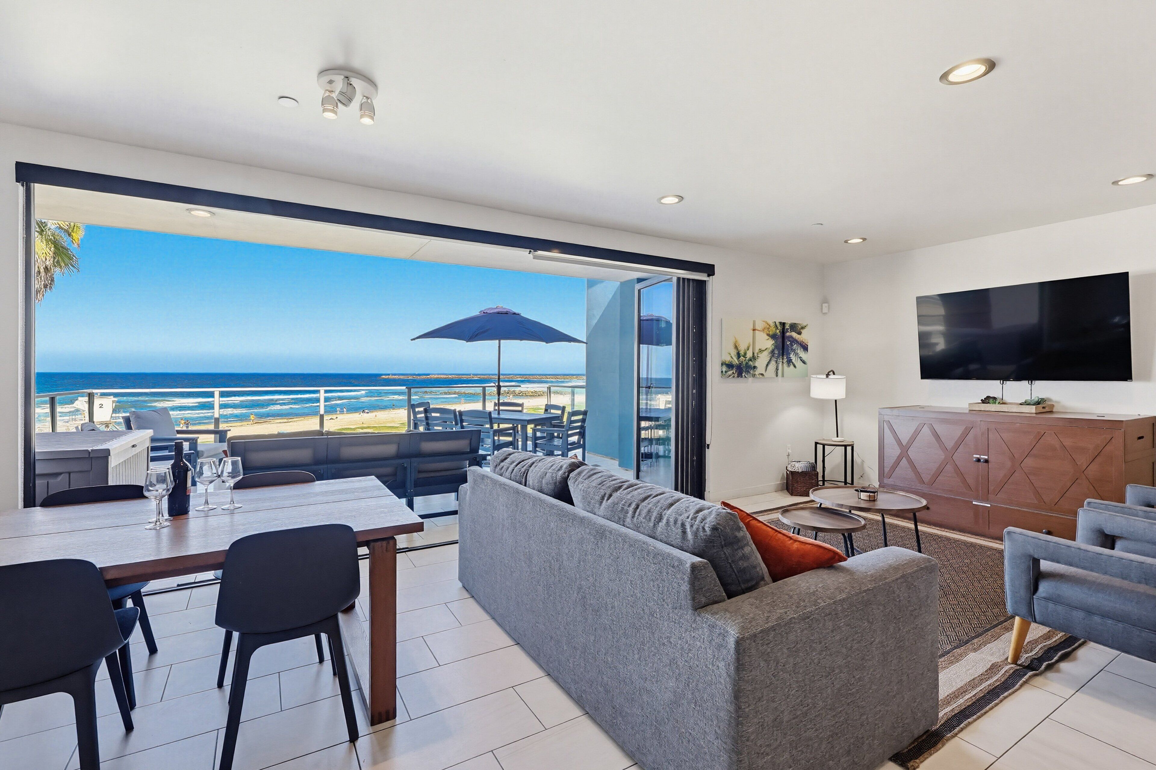 A modern living area with a sofa, dining table, and chairs, a flat-screen TV, and a view of the ocean.
