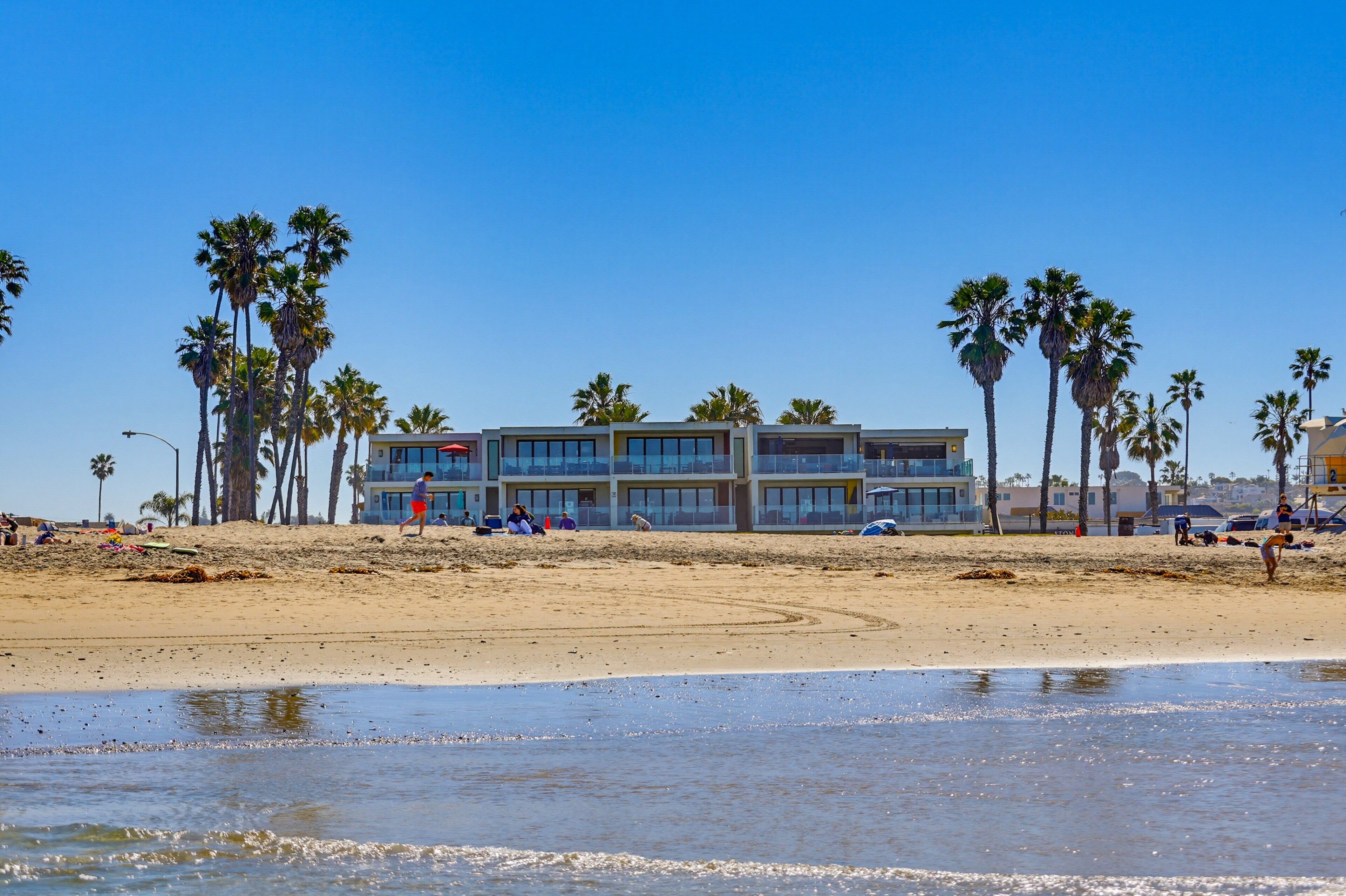 A beachfront hotel with multiple balconies, palm trees, and a sandy beach.