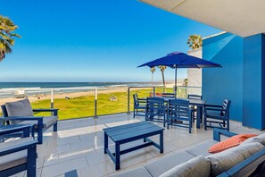 A balcony with a view of the beach, a table with chairs, and a blue umbrella. - Ocean Park 09 (San Diego)